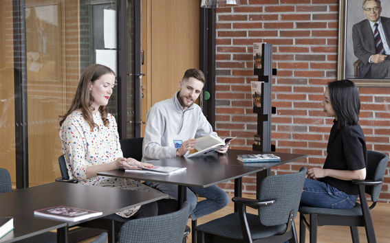 Kolme opiskelijaa tutkimassa lehtiä pöydän ääressä. Kuva: Aalto-yliopisto / Roope Kiviranta