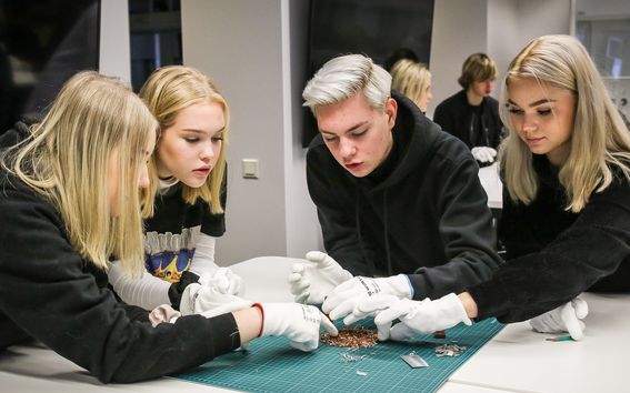 Neljä nuorta tutkii metallin paloja suoja hanskat kädessä pöydän ääressä