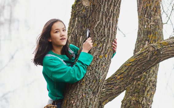 Girl sitting on a tree with a magnifying glass