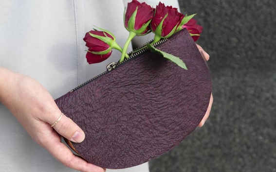 Colour photo showing a dark brown/aubergine coloured clutch purse held in two hands with Roses coming out of the zippered top