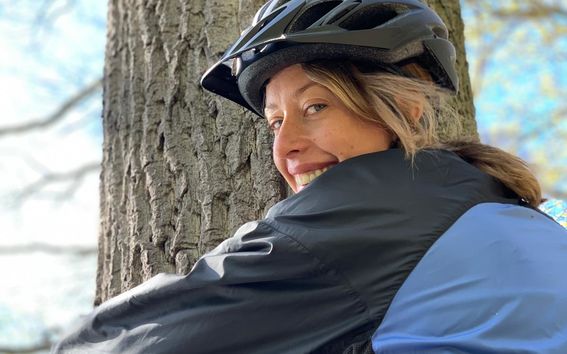 Carolina Weigl happily hugging a tree wearing a blue outdoor jacket and a bike helmet.