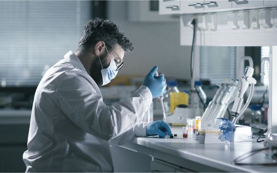 Photo shows chemistry researcher in a white lab coat wearing blue gloves working in the laboratory with a pipette.