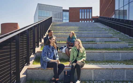Four people sitting on the stairs near School of Business and Väre, in sunlight