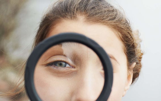 A girl with brown hair looking through a magnifying glass 