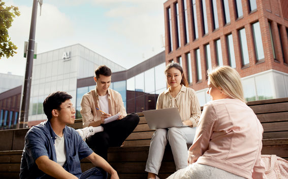 Four students sitting in front of Väre building studying and discussing