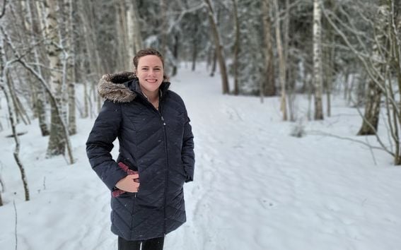 Cordelia in a blue winter jacket, pictured smiling with a snowy forest in the background.