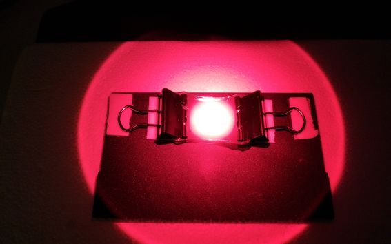 A gel being lit by a bright red light and stretched between two clips. 