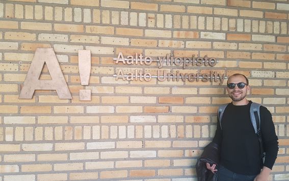 Jonathan Kahati wearing sunglasses and a backpack standing in front of Aalto Universitu School of Business building.