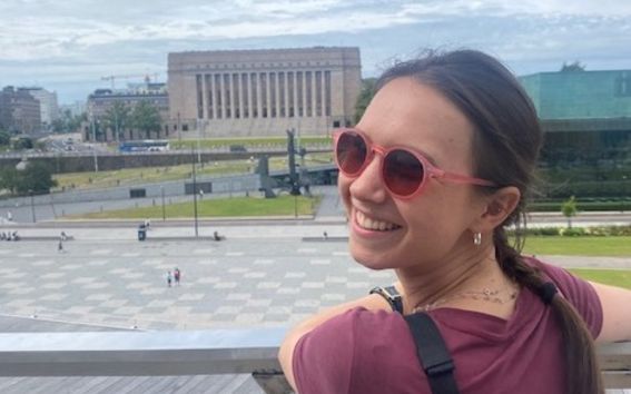 Liva Gramlow in sunglasses, smiling towards the camera in front of the Parliament House in Helsinki.