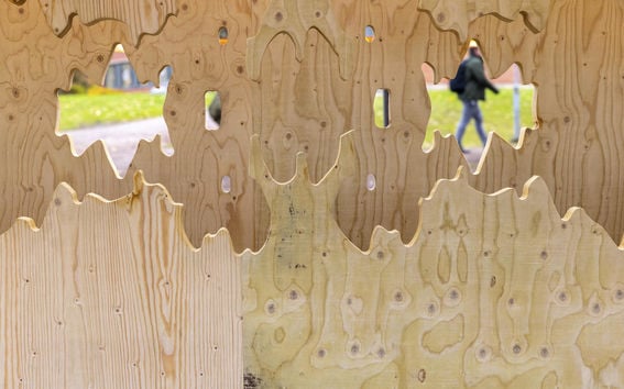 A view through a plywood outdoor art, a person walking in the distance.