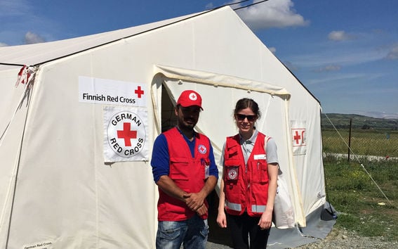 Kuvassa Saara Hietanen seisoo kollegansa kanssa Punaisen Ristin teltan edessä, kun hän työskentelu ulkomailla hätäaputehtävissä.