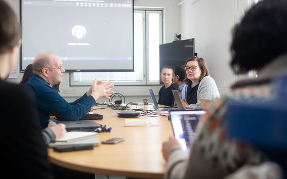 Researchers having a discussion in a meeting room with their laptops open on the table 