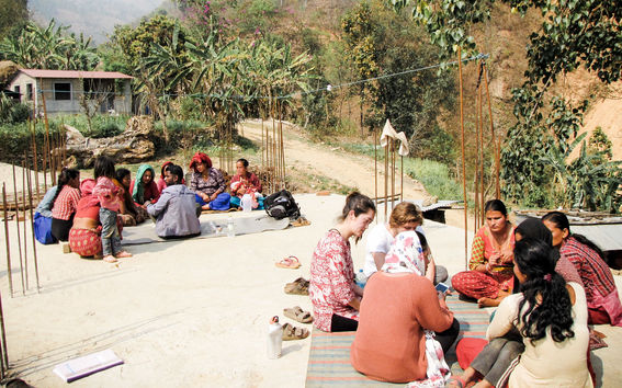 Humanitarian architects at field work in Nepal, sitting on rugs and discussing with local people
