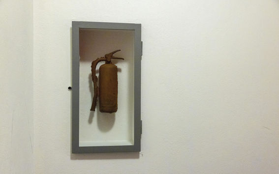 Kaisaleena Halinen's artworks show fire extinguishers in four different materials, here in rusty metal, in a casing in an indoor staircase in the K1 building.