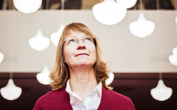 A woman in red cardigan looking up, with white lamps in the background.