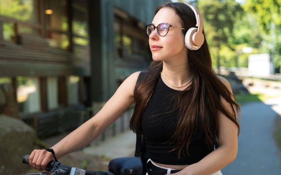 Henkilö taluttaa polkupyörää kuulokkeet päässä ja katsoo mietteliäästi kaukaisuuteen.