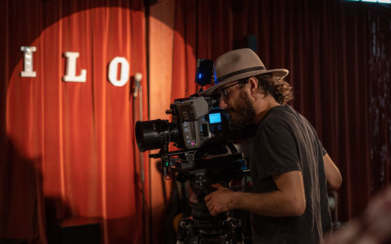 A student in a hat filming in front of a red curtain.