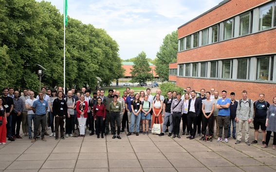 A group of several dozen people pose for a photo outside at Aalto University.