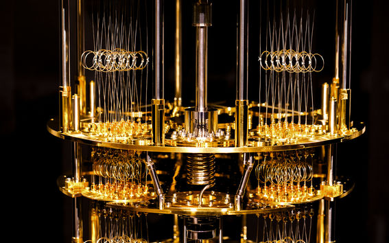 An illuminated gold-plated cryostat built by Bluefors sits on a black background.