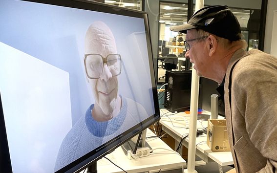 Mies katsoo kuvaruutua, josta hän katsoo takaisin virtuaalinen Kekkonen.