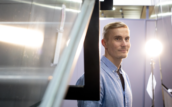 Doctoral researcher Lassi Meronen dressed in a blue shirt, photographed from the side with a studio light shining on the right side of the photo