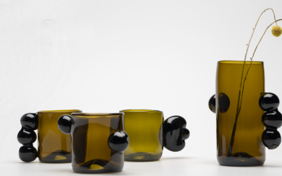 A collection of dark green-brownish glass mugs and a vase with blob like ornamental handles