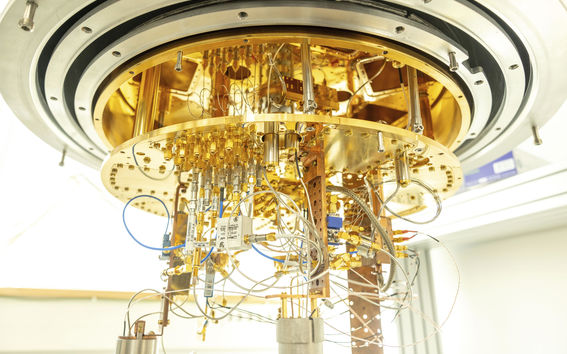 A gold-plated cryostat sits half open with many cables coming out from the bottom.