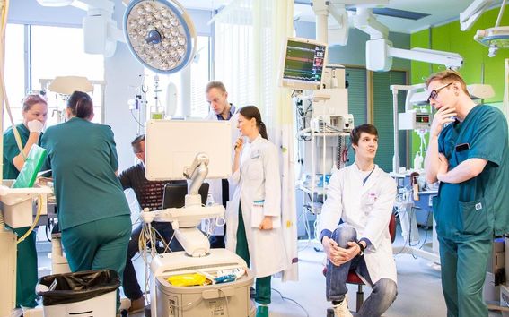 Seitsemän henkilöä sairaalassa laboratoriotakit yllään lääketieteellisten laitteiden ympäröiminä