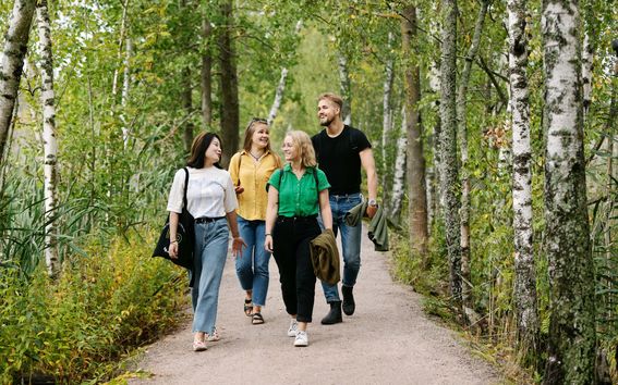 Group of four students walking in a path in a Finnish forest.