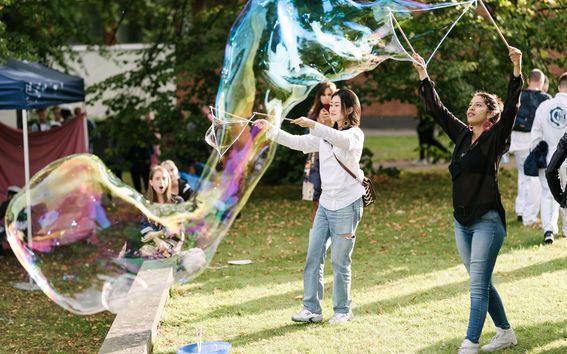 Two women making big bubbles with sticks on the grass.