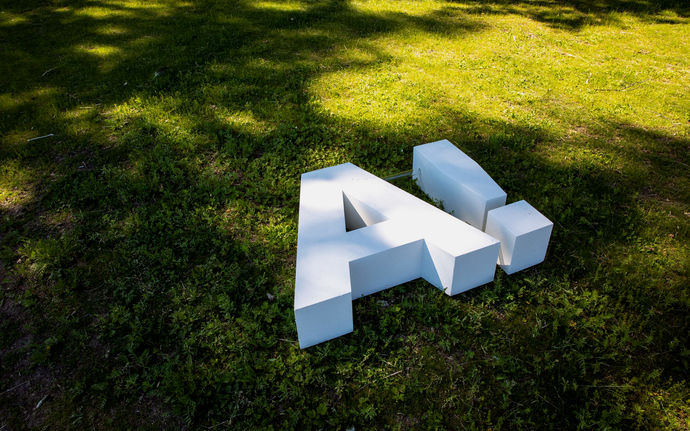 Aalto-yliopiston valkoinen 3D-logo, iso A huutomerkillä, kampuksen nurmikolla / kuvaaja Mikko Raskinen, Aalto-yliopisto