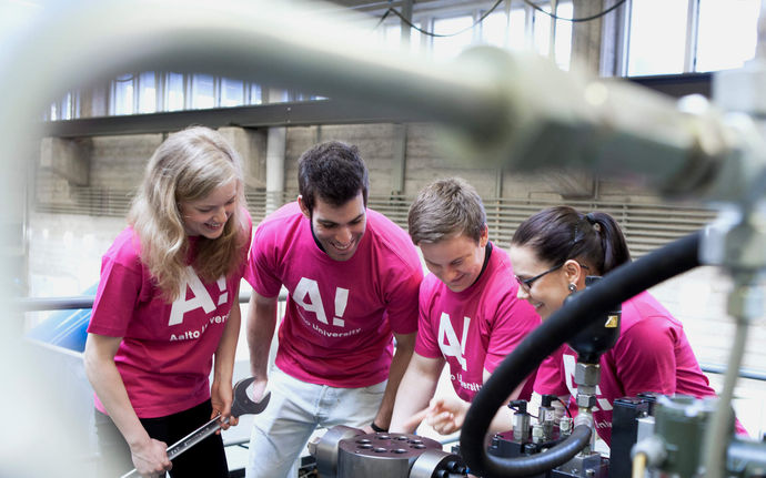 Four engineering scientists in pink t-shirts in front of an an engine
