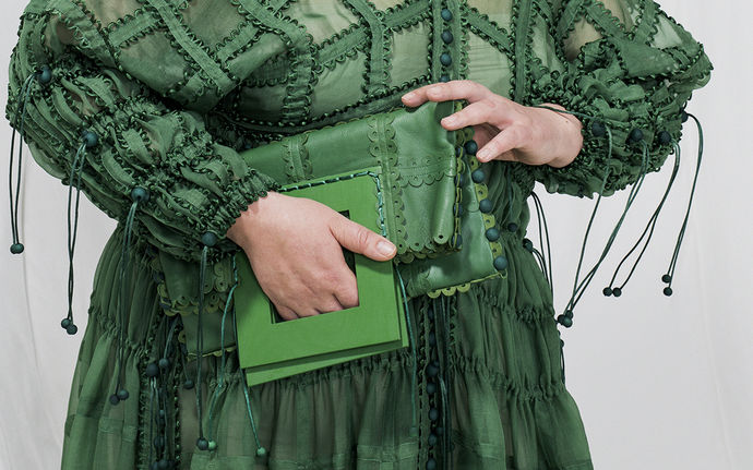 A hand holding green purse on top of a green dress