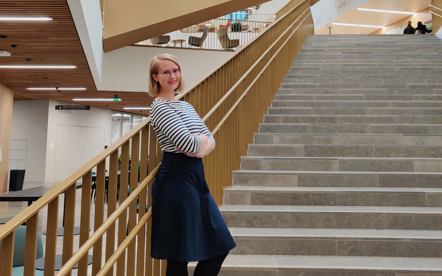 Petra Fagerlund standing on the tall staircase in the School of Business lobby, smiling and leaning against the railing.