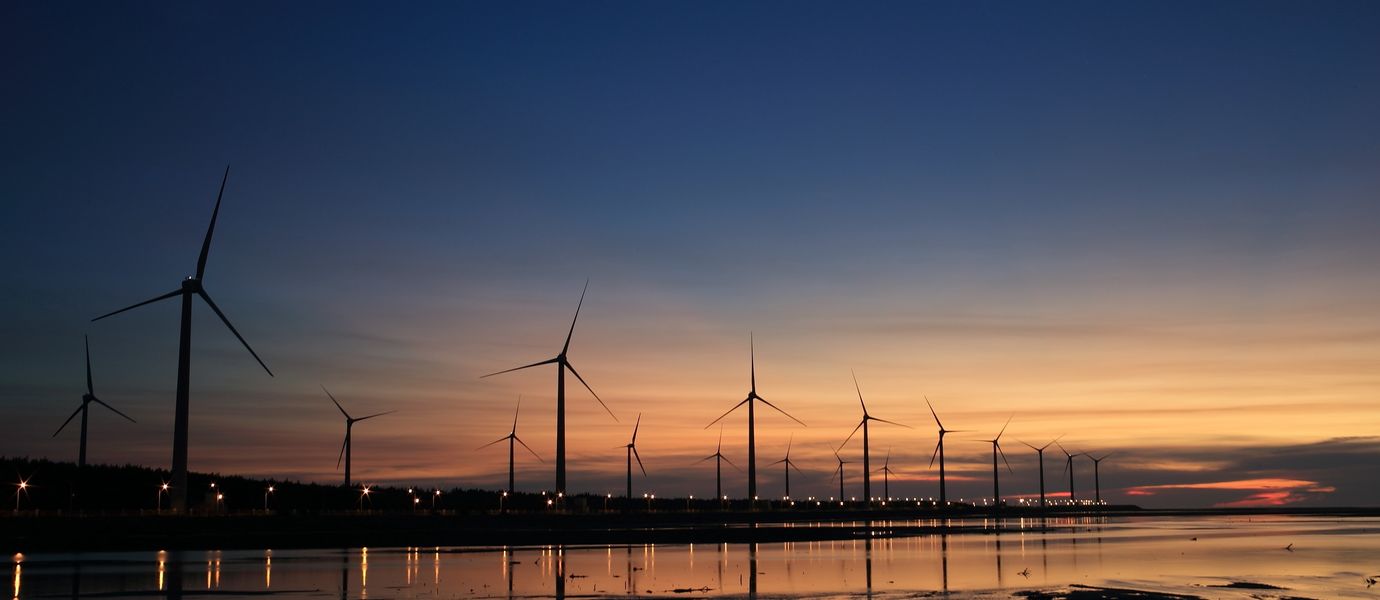 Wind farm by the water at sunset.