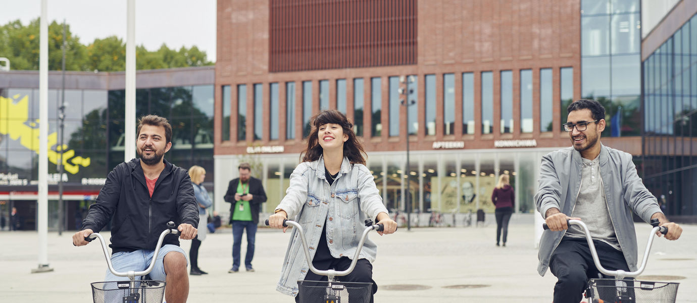 Thre students bicycling in front of the Väre building.