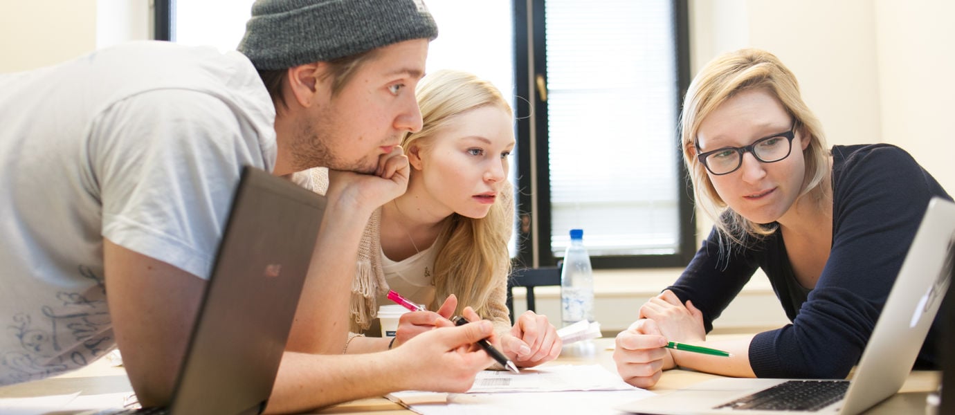 Three Aalto University students lean over a table looking at a laptop screen.