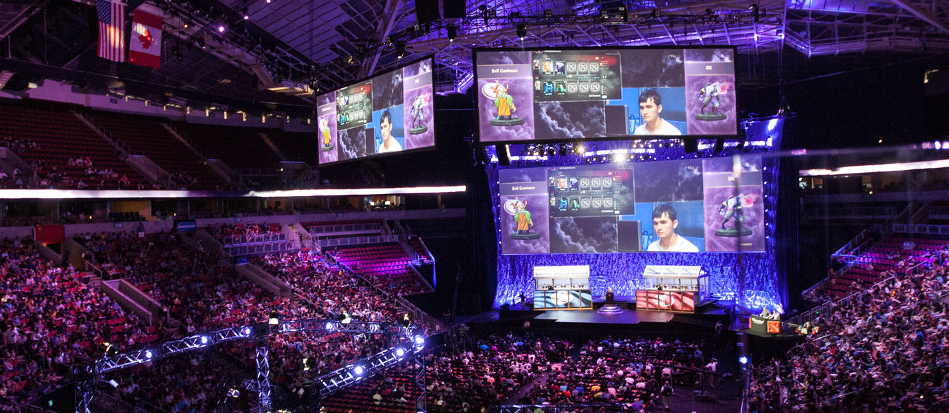 Large arena filled with a crowd watching a game of DOTA2 projected on big screens