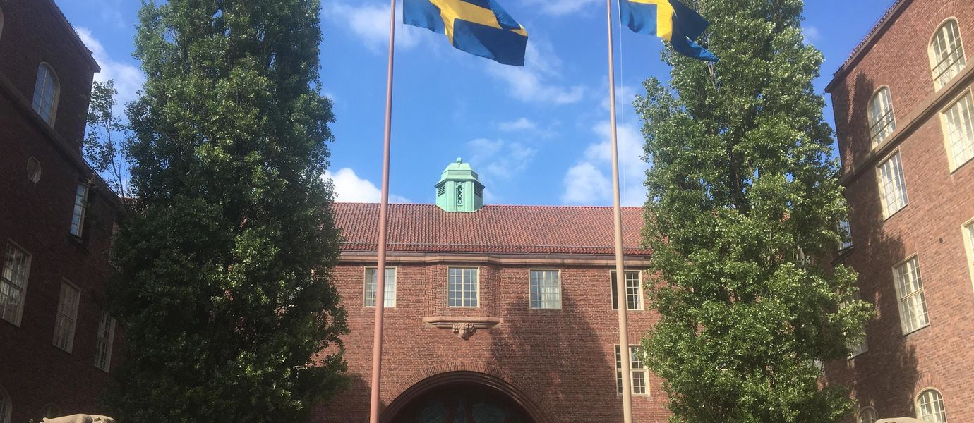 Swedish flags flying on KTH campus gates, building behind is of red brick