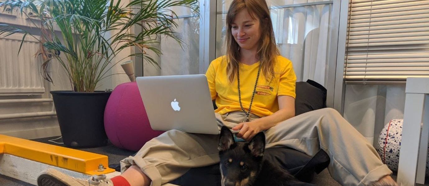 Salla-Mari Saanio sitting relaxedly by a laptop with a puppy on her feet.