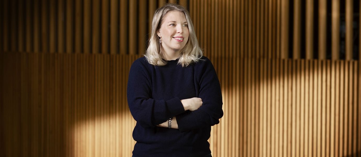 Johanna Fagerström pictured with her arms crossed in a blue knitted sweater. She is smiling and looking at something behind the photographer.