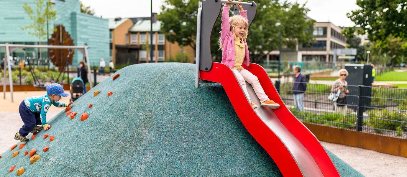 Kuvassa lapsi liukuu alas liukumäkeä leikkipuistossa kaupunkiympäristössä.