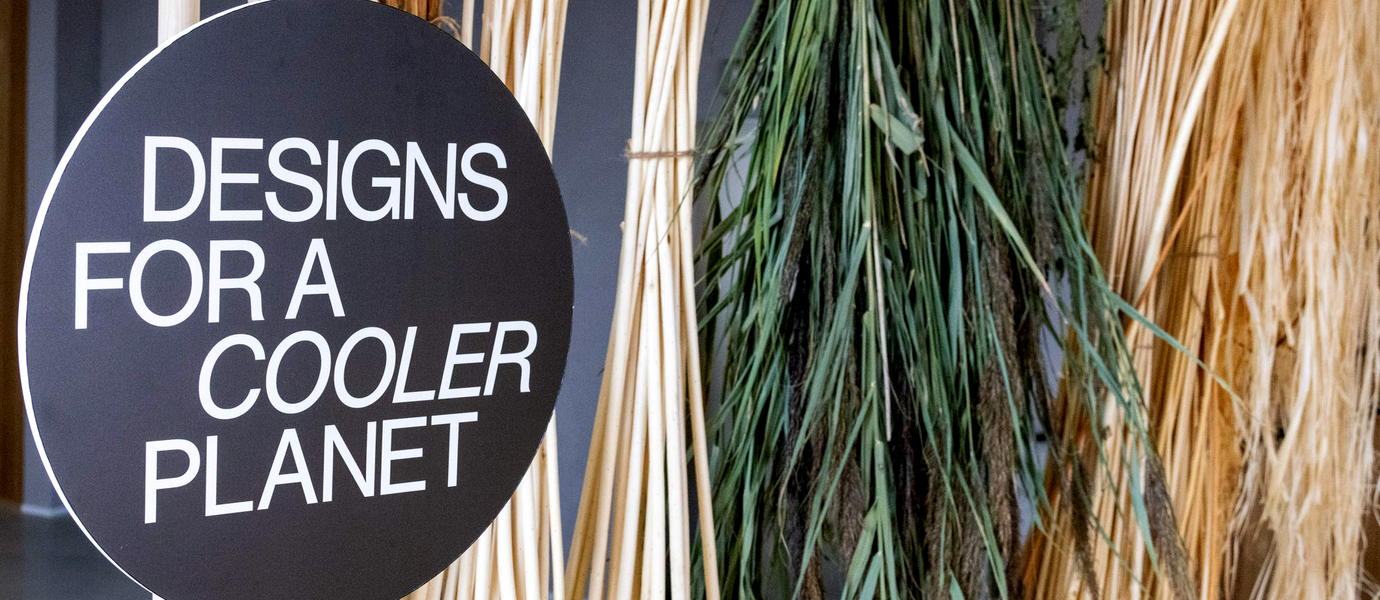 Photo of round black sign with white letters "Designs for a cooler planet" with dried reeds and grasses