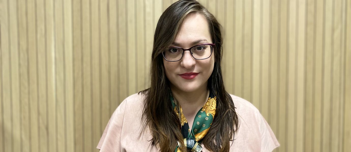 Marcela looking straight into the camera wearing a pink t-shirt and a patterned scarf, red lipstick and glasses.