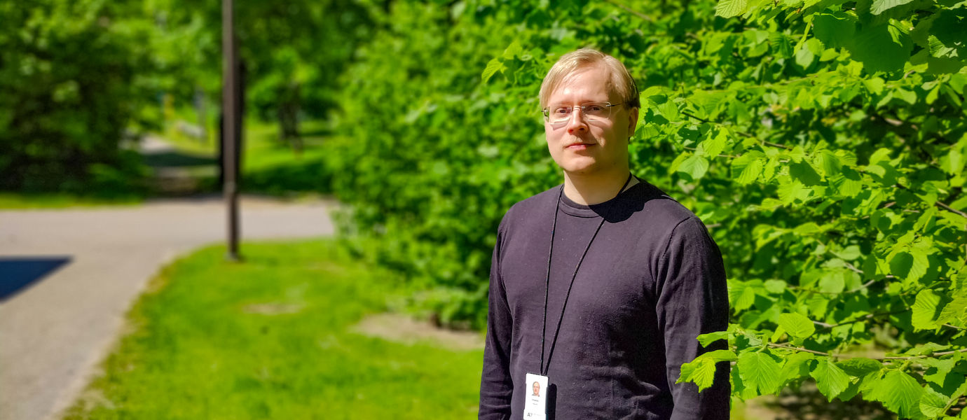 Heikki Nurmi outdoors on a sunny day in a black shirt in front of a background of leaves and trees.