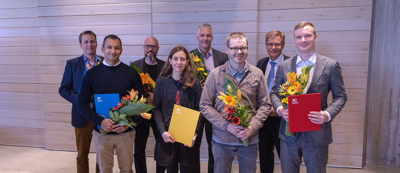 A group of eight Aalto people awarded in Aalto Day One, standing and holding flower bouquets