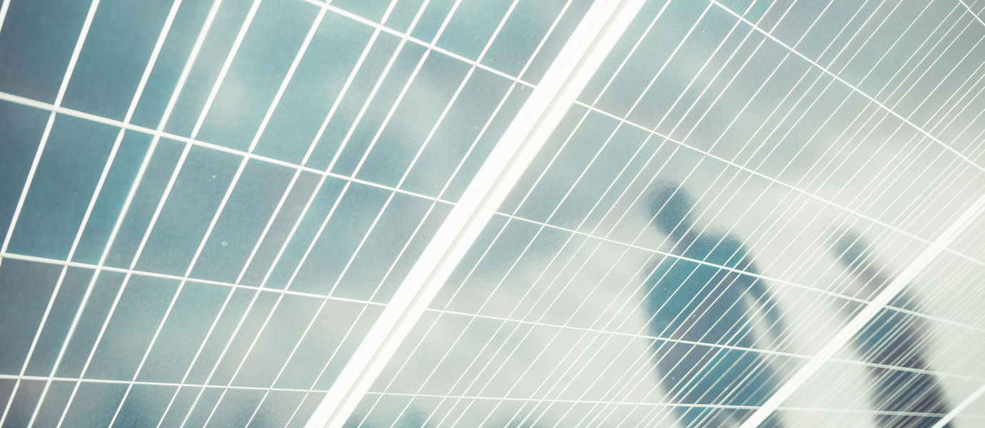 Reflections of two people on solar panels. Light blue sky is reflected on the background.