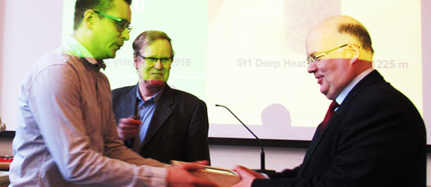 Palkintoa luovuttamassa St1 Deep Heat Oy:n teknologiajohtaja Rami Niemi ja professori Raimo Lovio. Palkintoesine on professori Lundin työpisteen alla Otaniemessä sijaitsevasta peruskalliosta, johon St1 poraa parhaillaan koereikää kaukolämmön keräämiseksi.