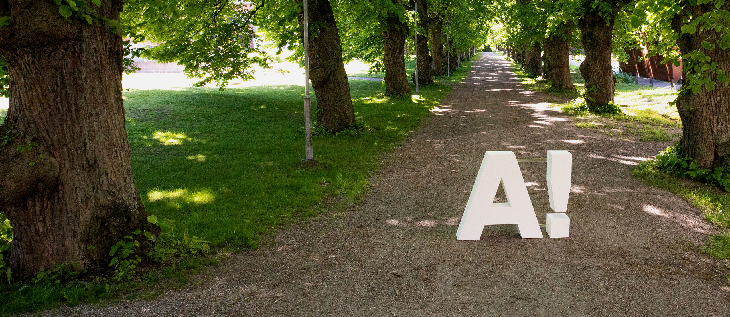 Yliopiston 3D-tulostettu logo hiekkatiellä kampuksella.