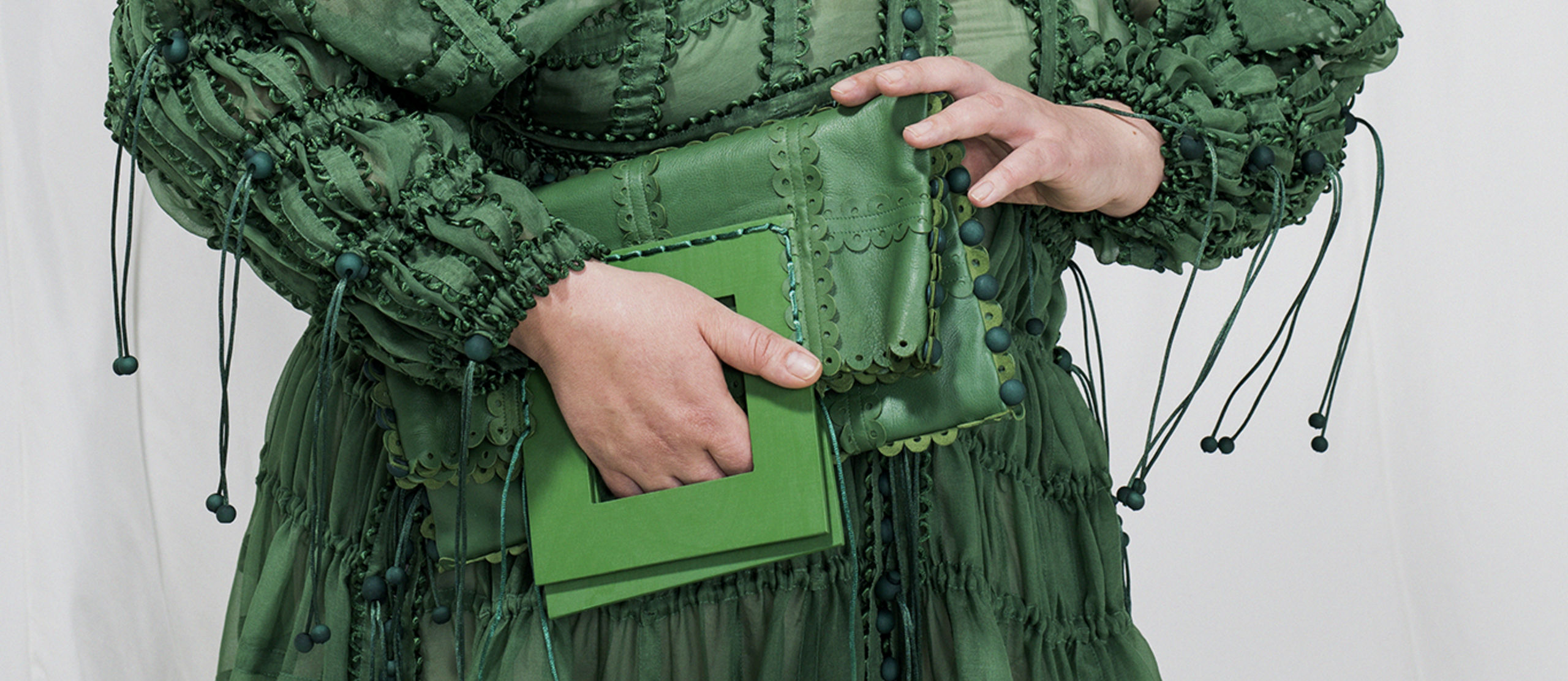A hand holding green purse on top of a green dress